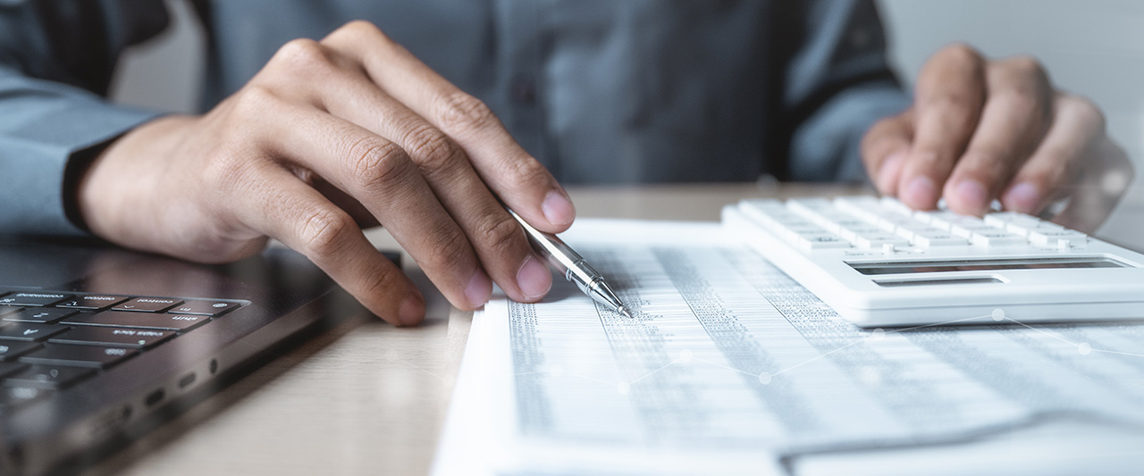 A male hand comparing a printed account record with digital records using a calculator