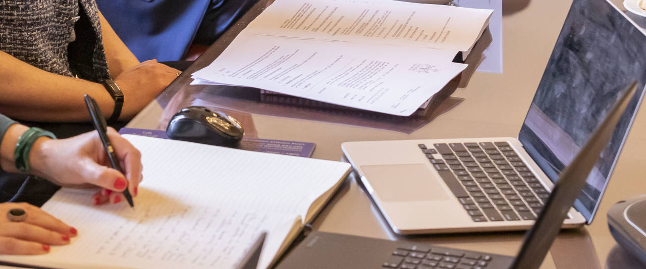 A female hand taking notes on paper in front of a computer